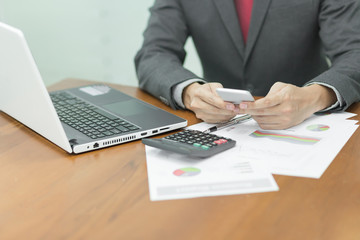 Selective focus Young business man working on a mobile phone ,laptop, document and calculator on the wooden desk in office.