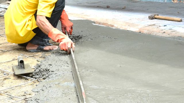Mason worker leveling concrete with long trowels