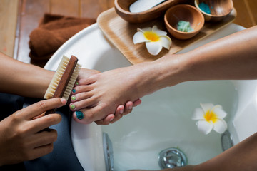 Manicure and pedicure series: Pedicurist brushing customer's foot in pedicure bowls