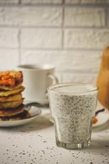 chia seeds with milk in a transparent glass, pancakes and a cup of tea - breakfast on a light background