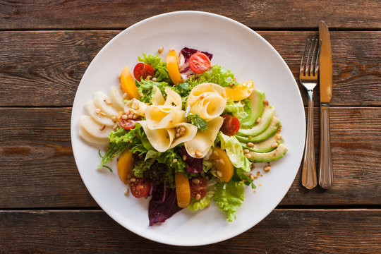 Lettuce salad with cheese and fruits on plate. Fresh vegetables decorated pine nuts, avocado, pearch and pear, serving in restaurant, top view