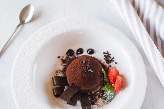 Delicious chocolate dessert on white plate with decoration from strawberry and mint. Fondant serving in restaurant for real gourmet