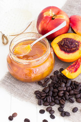 Nectarine (Peach, Apricot) coffee jam confiture in glass jar and spoon on white wooden background. Vertical. Selective focus. Copy space for your text.