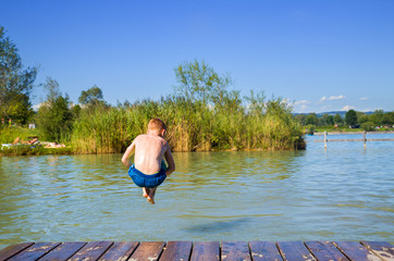 Fototapeta na wymiar Young happy boy is jumping into a lake on a sunny and bright day in Austria