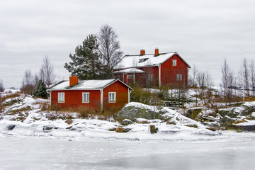 Red wooden house on an island covered in snow during winter in Helsinki, Finland.