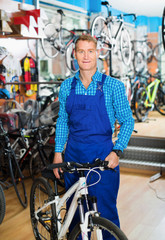 Fototapeta na wymiar Positive male seller in uniform holding new bicycle