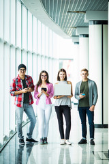 Happy four friends standing and using modern gadgets indoors