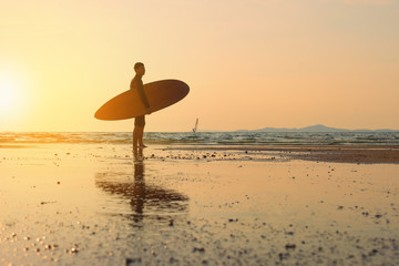 Man playing surfboard on the beach at sunset.