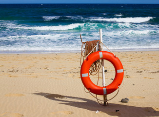 Swimming circle. Life buoy red color on beach with bright sand and sky background. Two warning signs. Safety guard, lifebuoy, lifeguard. Vacation at ocean.