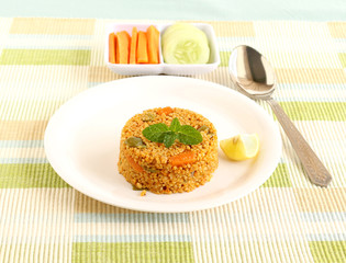 Healthy food quinoa pilaf, and in the background is the tray with raw carrot and cucumber.