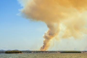 rising smoke from forest fire behind city Biograd on the sea at Croatian coast