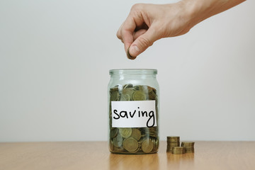 Distribution of cash savings concept. Hand puts coins to the glass money boxes with inscription 'saving'.