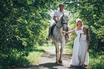 Man, woman dressed as a bride, girl and white horse in the park 