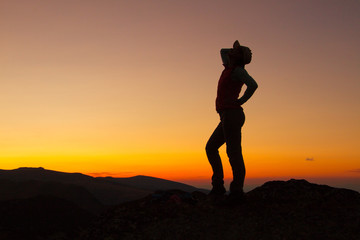 Fototapeta premium Silhouette of happy joyful young attractive woman jumping and having fun at the mountain against the sunset. Freedom, adventure and leisure vacation concept.