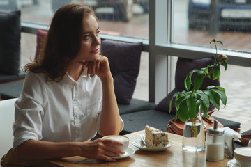 The girl enjoys a fragrant coffee and sweet cake sitting in a cafe. Business woman resting during break