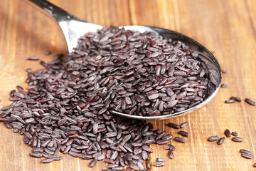 Black rice in a spoon, close-up, wooden background, horizontal, selective focus, high contrast