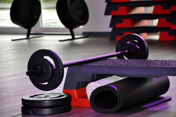 Langhanteltraining: die Sportartikel wie Langhanteln, Gewichtsscheiben und Stepper für Kraft und Ausdauersport in einem Fitnesstudio.