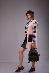 Portrait of extraordinary woman dressed in black hat and plaid shirt staying over gray backgro