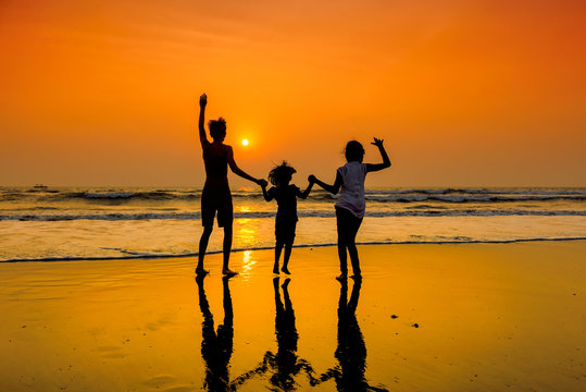 Silhouettes Of Group Of Happy Children Dancing On Beach At Sunset.