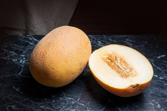 Whole and half honeydew melon fruit on dark marble background.