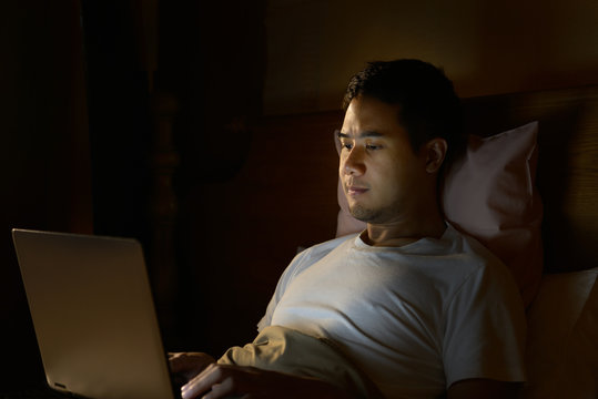 Young Man Using Laptop Computer In His Bed At Night