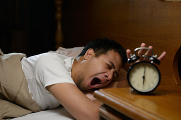 Young man turning off the alarm clock on the bed