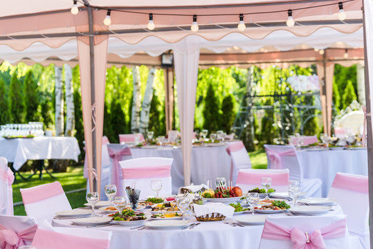 Served round banquet table outdoor in marquee decorated pink flowers and silk