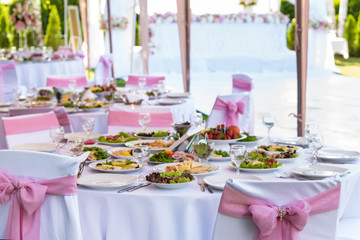 Served round banquet table outdoor in marquee decorated pink flowers and silk