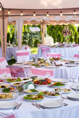 Served round banquet table outdoor in marquee decorated pink flowers and silk