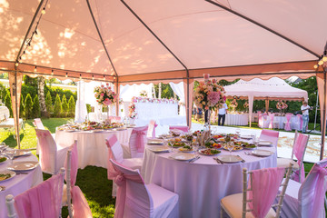 Served round banquet table outdoor in marquee decorated pink flowers and silk