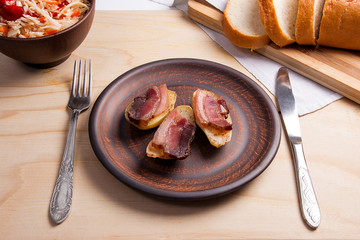 Baked potatoes with slices of bacon and eating utensils on wooden background. Sauerkraut in clay bowl and slices of white bread on cutting board..