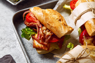 Fresh baguette sandwich bahn-mi styled. Bacon, roasted cheese, tomatoes and lettuce on metallic background. Close up