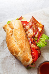 Fresh baguette sandwich bahn-mi styled. Bacon, roasted cheese, tomatoes and lettuce on metallic background. Close up view