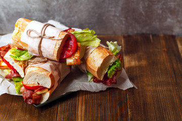 Fresh baguette sandwiches bahn-mi styled with bacon, roasted cheese, tomatoes and lettuce on wooden background. Horizontal composition, text space on the right.