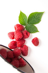 White cup with ripe raspberries and green leaf isolated on white background.