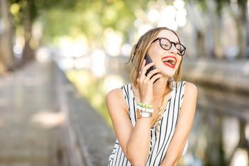 Young smiling business woman talking with smartphone outdoors at the park during the sunny day