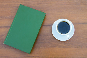 Cup of coffee and closed book on wooden table