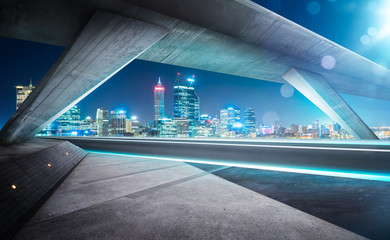 Empty asphalt road under the bridge during the night with beautiful city skyline background .