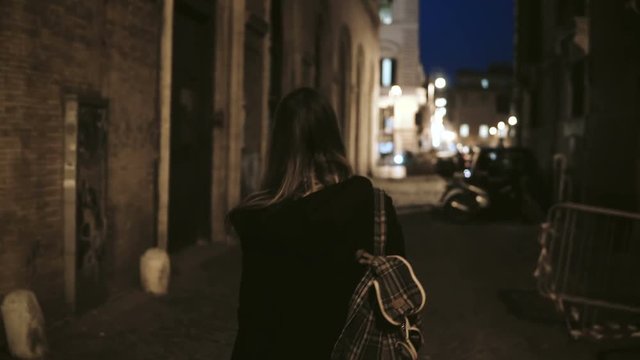 Back view of young tourist woman walking through the deserted lane without people to downtown in the evening.