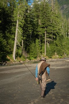 Rear view of man with fishing rod walking on sand