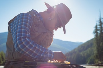 Man removing fishing bait from box while sitting against sky