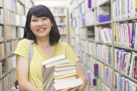 Female College Student Carrying Pile of Books in Library