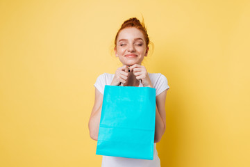 Fototapeta premium Pleased ginger woman holding packet in hands with closed eyes
