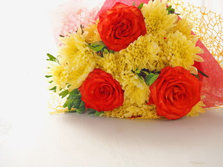 Greeting card. Yellow and red flowers upon white wooden background. Selective focus on the front. Copy space for your text.