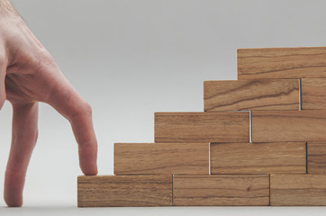 Persons hand walking up a set of  wooden blocks. Business development and growth concept