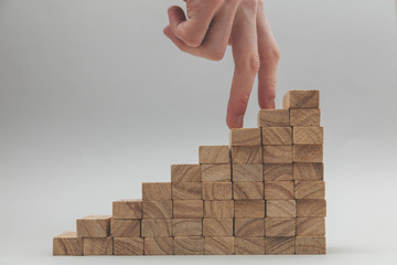 Persons hand walking up a set of  wooden blocks. Business development and growth concept