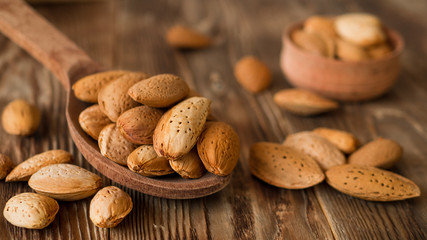 Almond in shells in wooden spoon and bowl on rustic table. Organic food for vegans. Food background