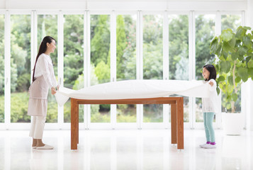 Mother and daughter spreading tablecloth on the table