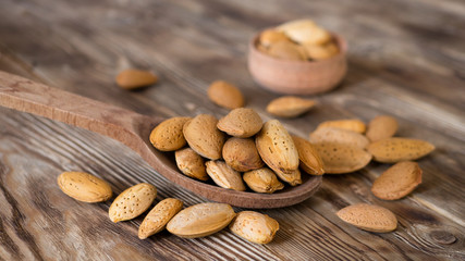 Raw almond in wooden spoon on rustic old table with soft focus