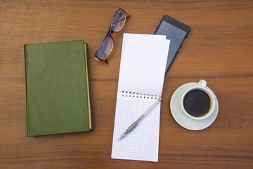 Cup of coffee, book, notepad, pen, eyeglasses and smart phone on wooden desk